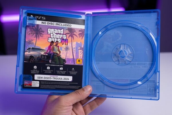 Mão segurando um estojo azul de PlayStation 5 aberto com a bandeja de disco totalmente vazia e um encarte de GTA 6 com o aviso NO DISC INCLUDED e voucher de download