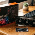 Placa de vídeo potente ao lado de caixa de placa-mãe ROG e SSD sobre mesa de madeira
