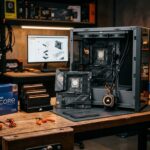 Bancada de montagem de PC Gamer com gabinete aberto, processador na caixa, módulos de memória RAM e water cooler