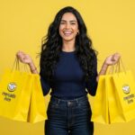 Mulher sorridente segurando sacolas amarelas de compras do Mercado Livre em fundo amarelo
