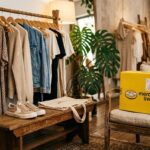 Arara de roupas moderna com vestidos e casacos ao lado de banco com tênis e caixa amarela do Mercado Livre