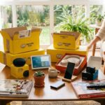 Sala de estar com caixas amarelas do Mercado Livre abertas sobre mesa com eletrônicos e gadgets